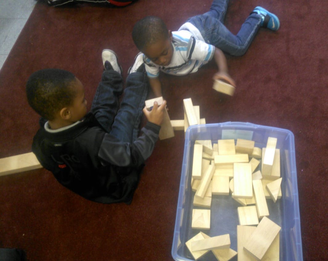Two children playing with wooden blocks on a floor