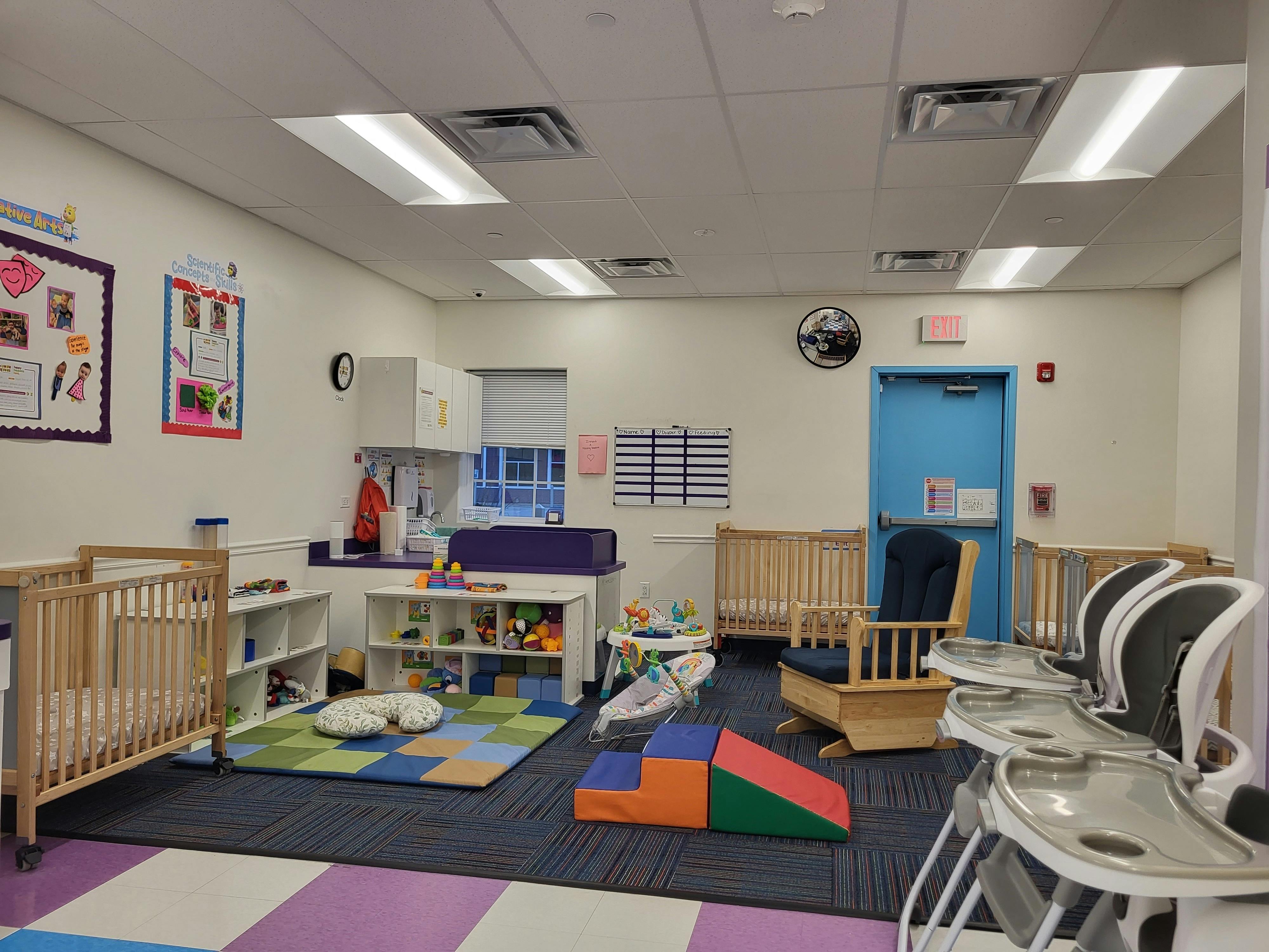 Infant room with cribs, changing table, play mat, and high chairs