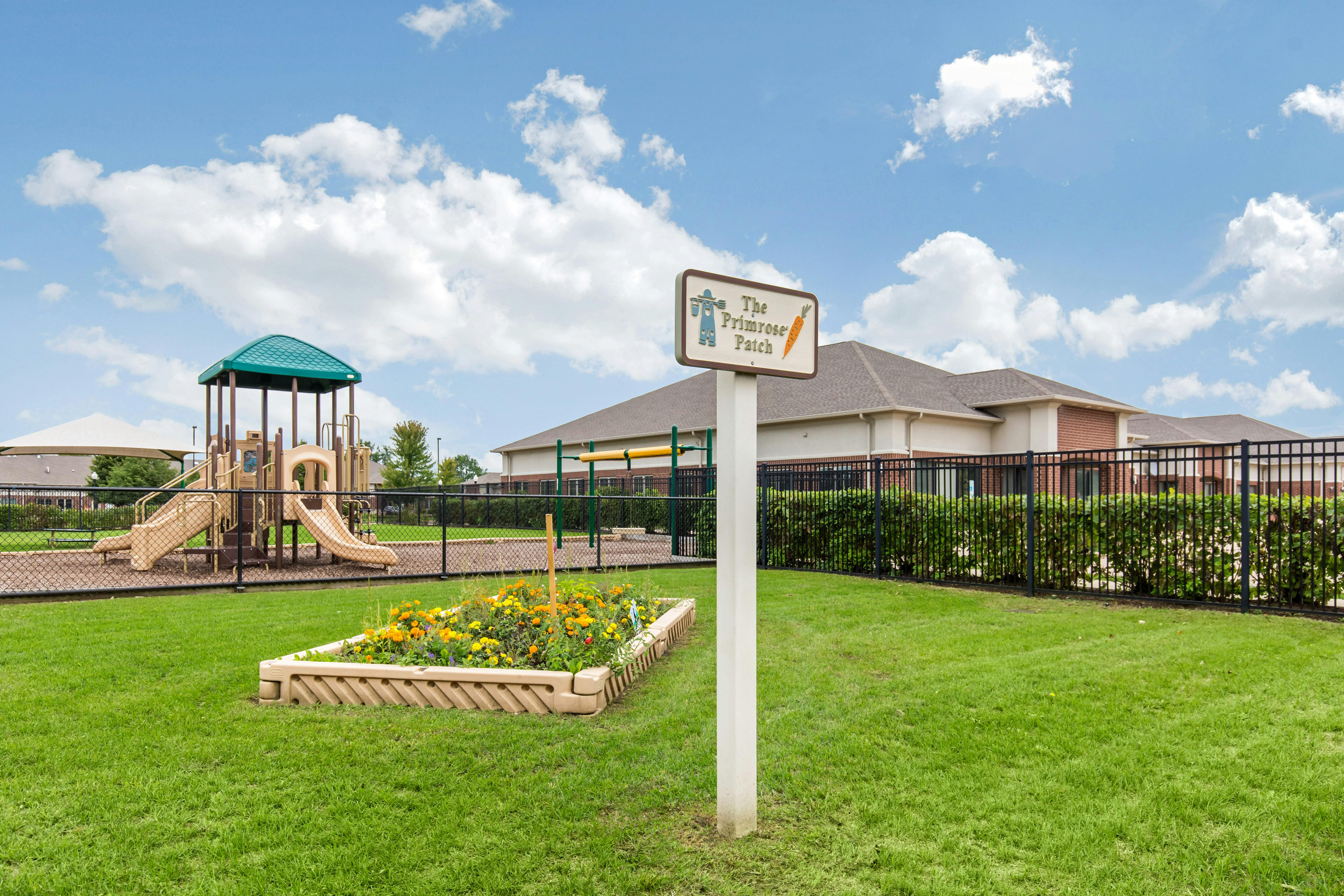 Playground area with a garden bed in the foreground and a sign reading "The Primrose Patch"