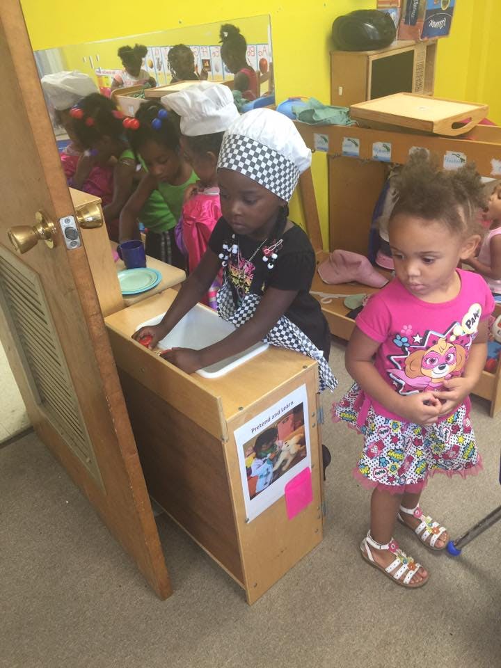 Child in chef hat and apron washing hands in a play sink