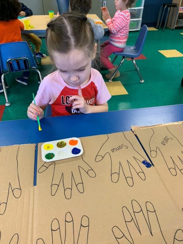Child painting hand outlines on cardboard in a classroom