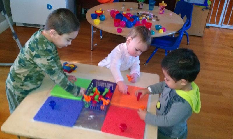 Three children playing with colorful blocks at a table