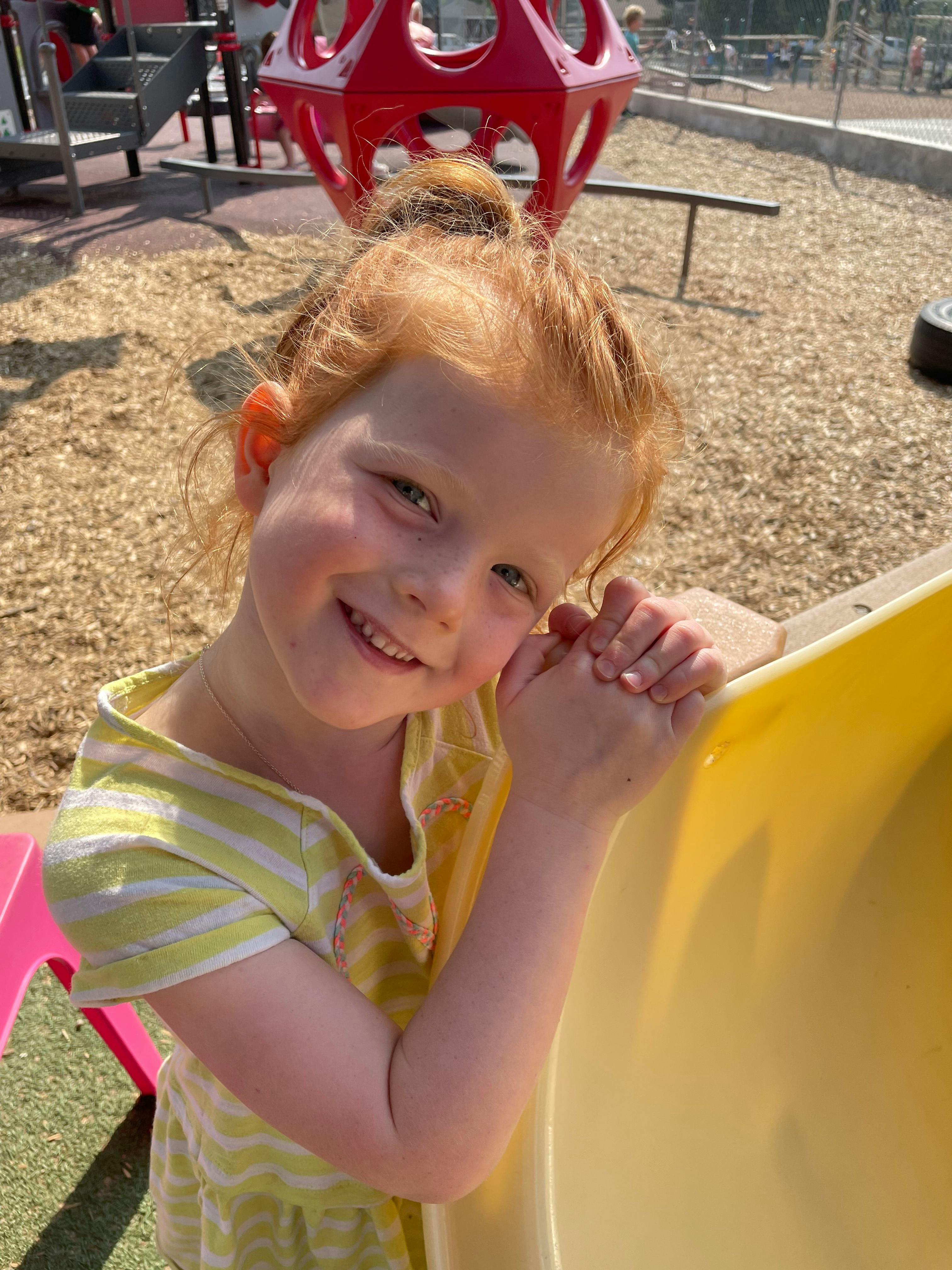 Child with red hair smiling at a playground