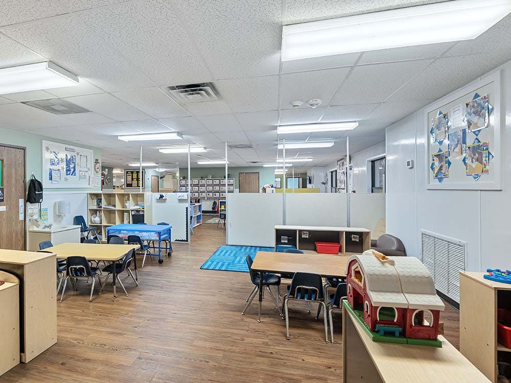 Empty classroom with small tables and chairs, shelves, and a toy barn
