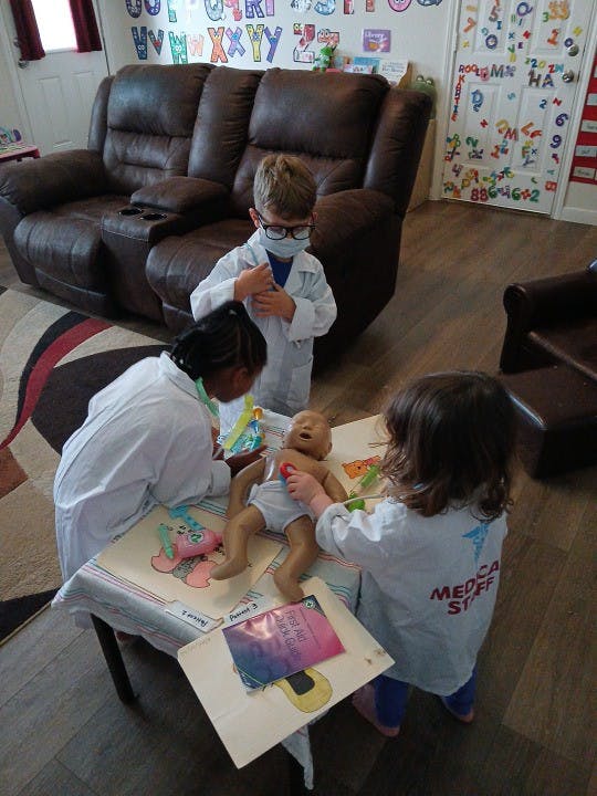 Three children in doctor costumes playing with a baby doll