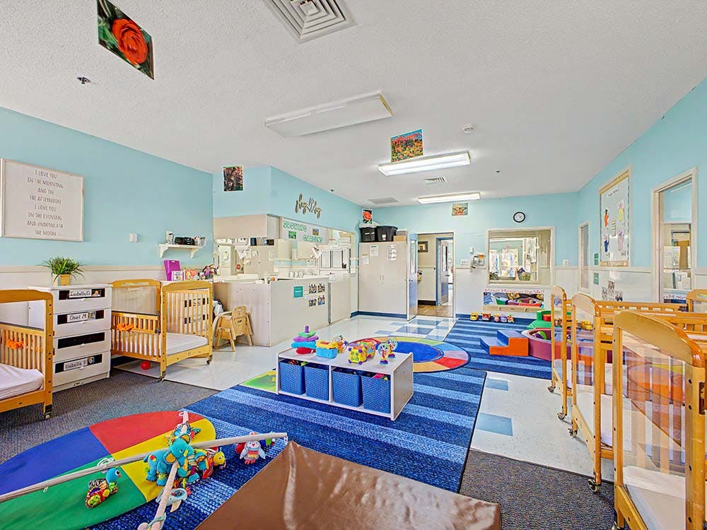 cribs in a daycare room with play mats and toys