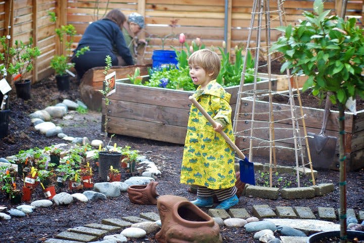 Child in yellow raincoat holding a shovel in a garden