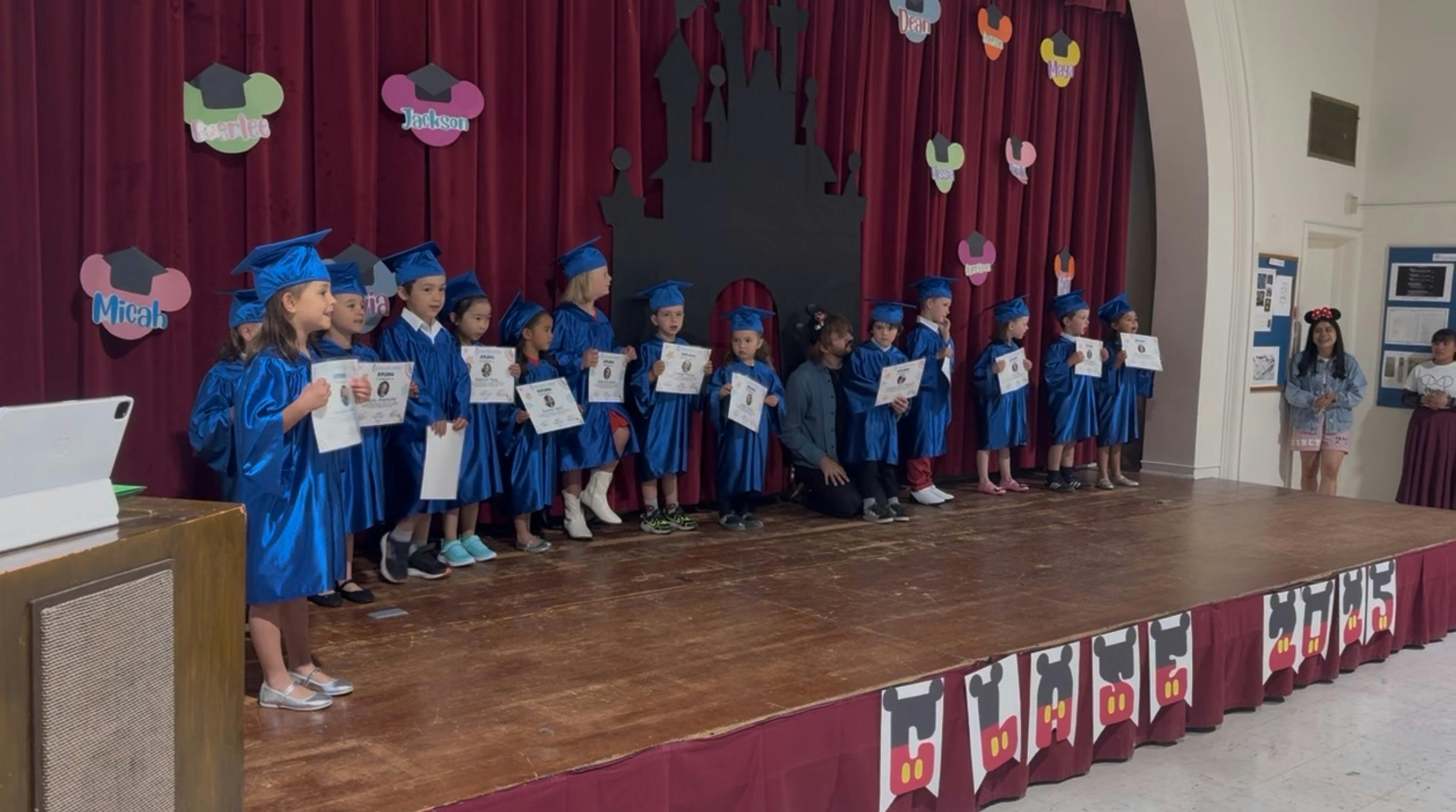 Children in blue graduation gowns and caps on a stage