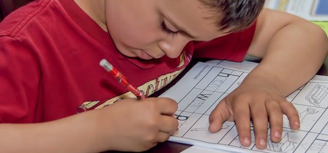 Child writing on a worksheet with a pencil