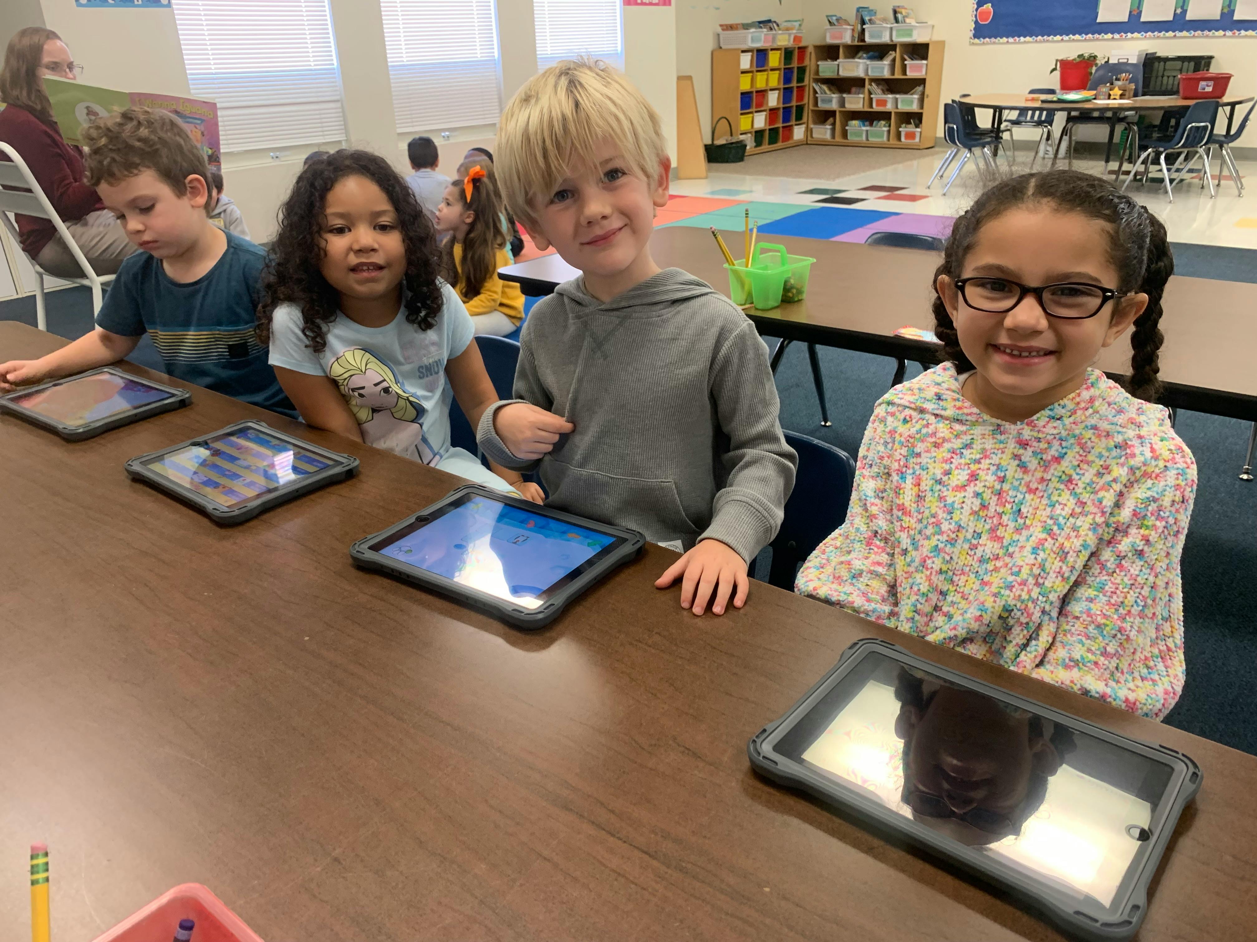 Children sitting at a table with tablets in a classroom