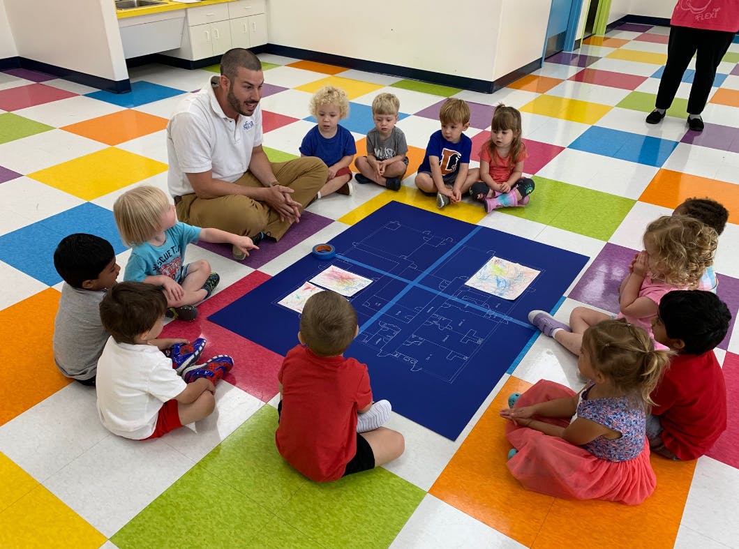 Adult and children sitting on a colorful floor looking at a blue mat