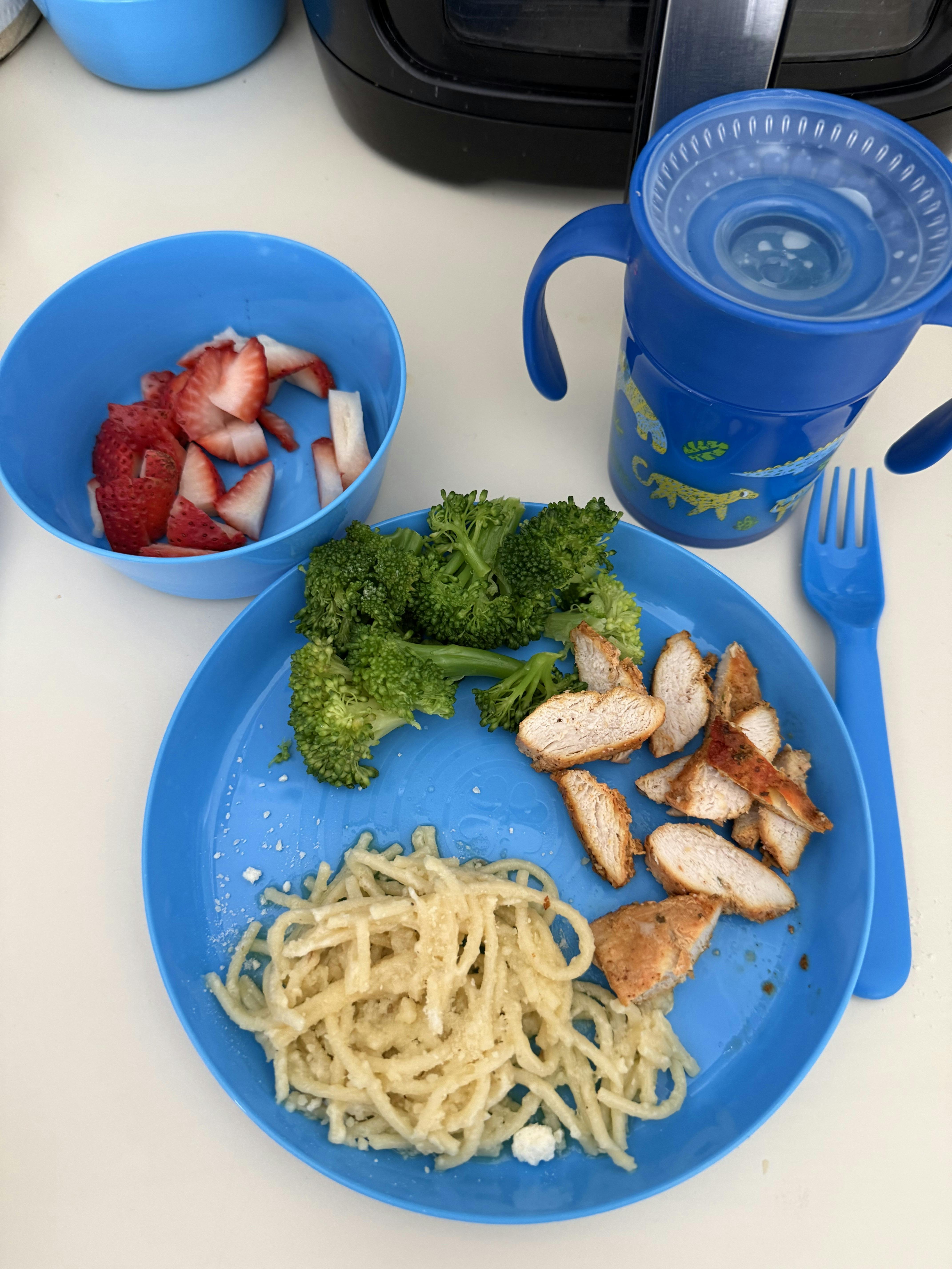 Child's meal with chicken, broccoli, pasta, and strawberries on a blue plate