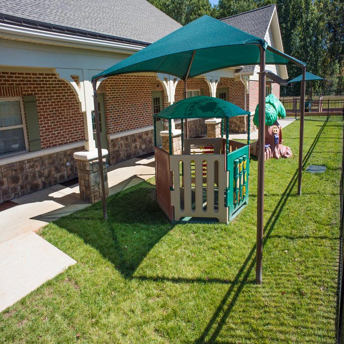 Play structure with a green canopy in a grassy area next to a building