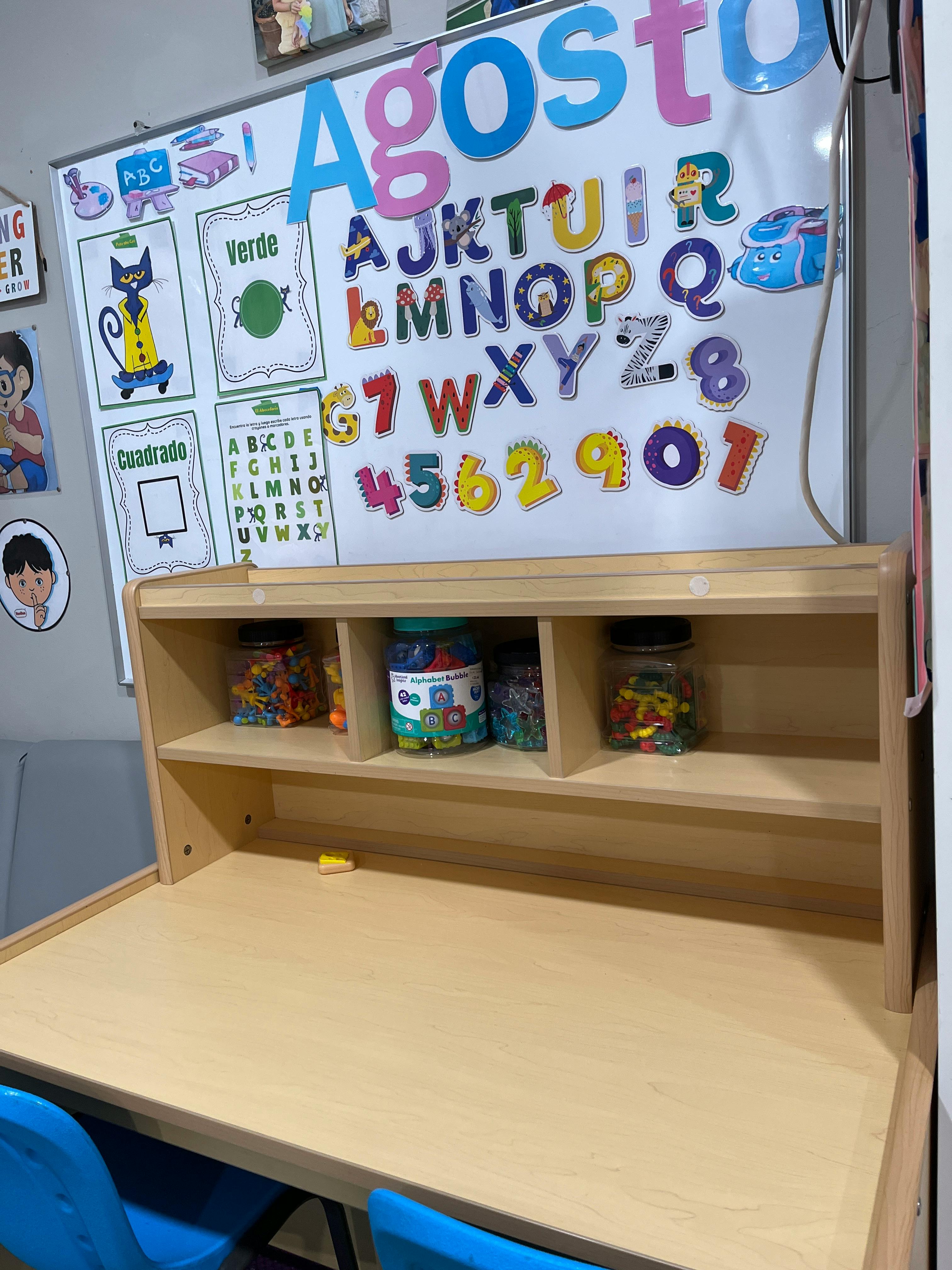 Classroom whiteboard with alphabet magnets and shelves containing jars of letters
