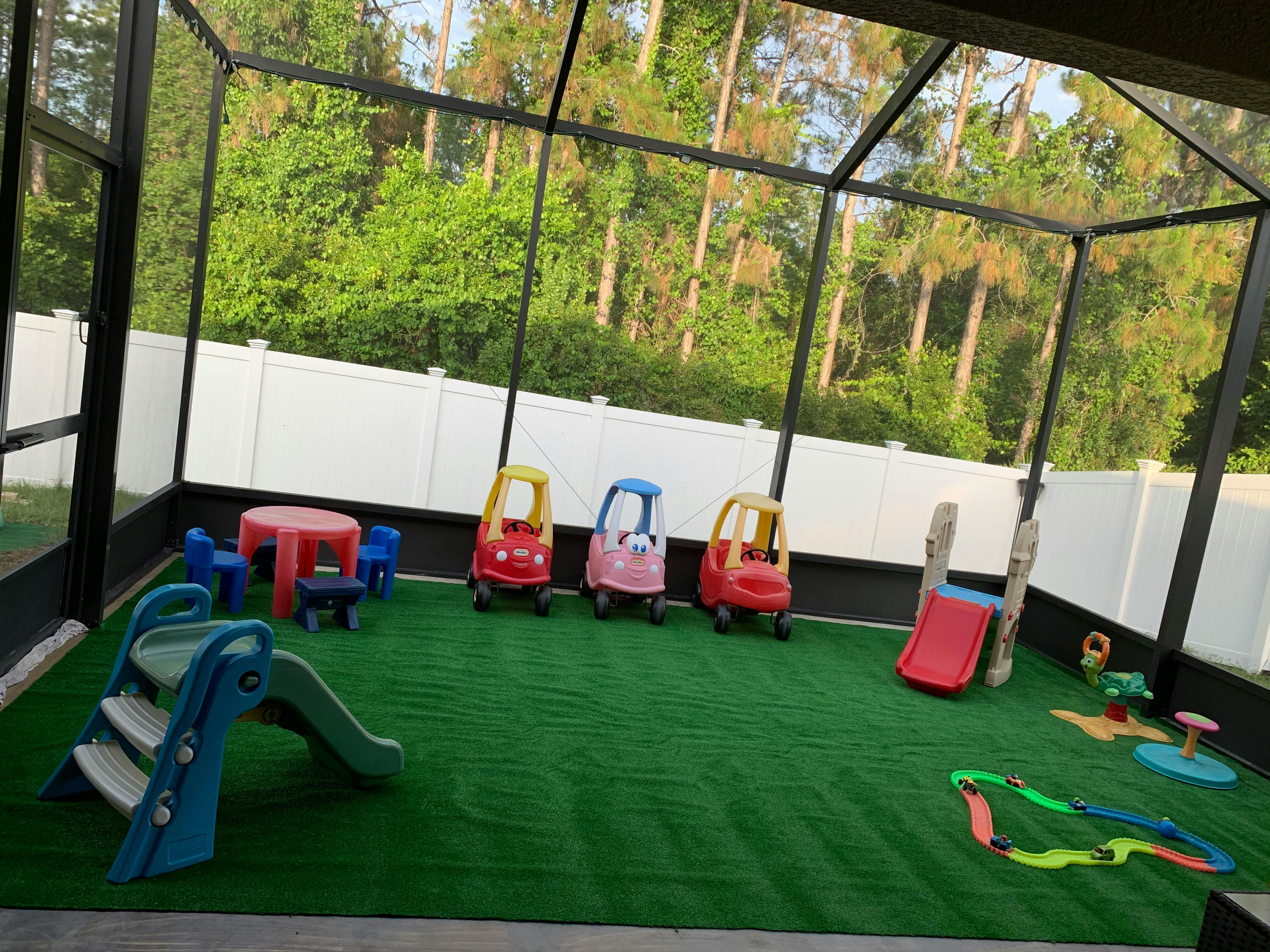 Screened-in patio with artificial turf, toy cars, slides, and a small table