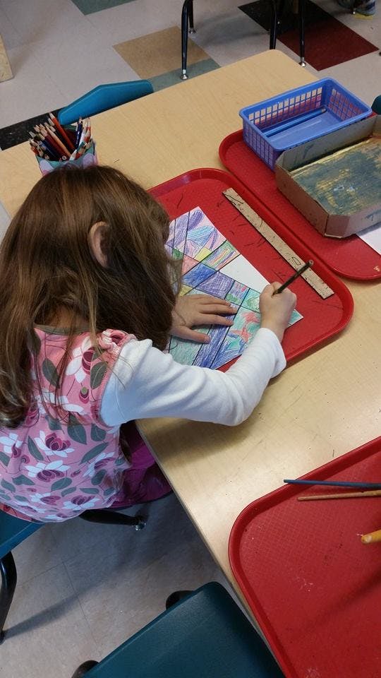 Child coloring a geometric pattern on paper at a table