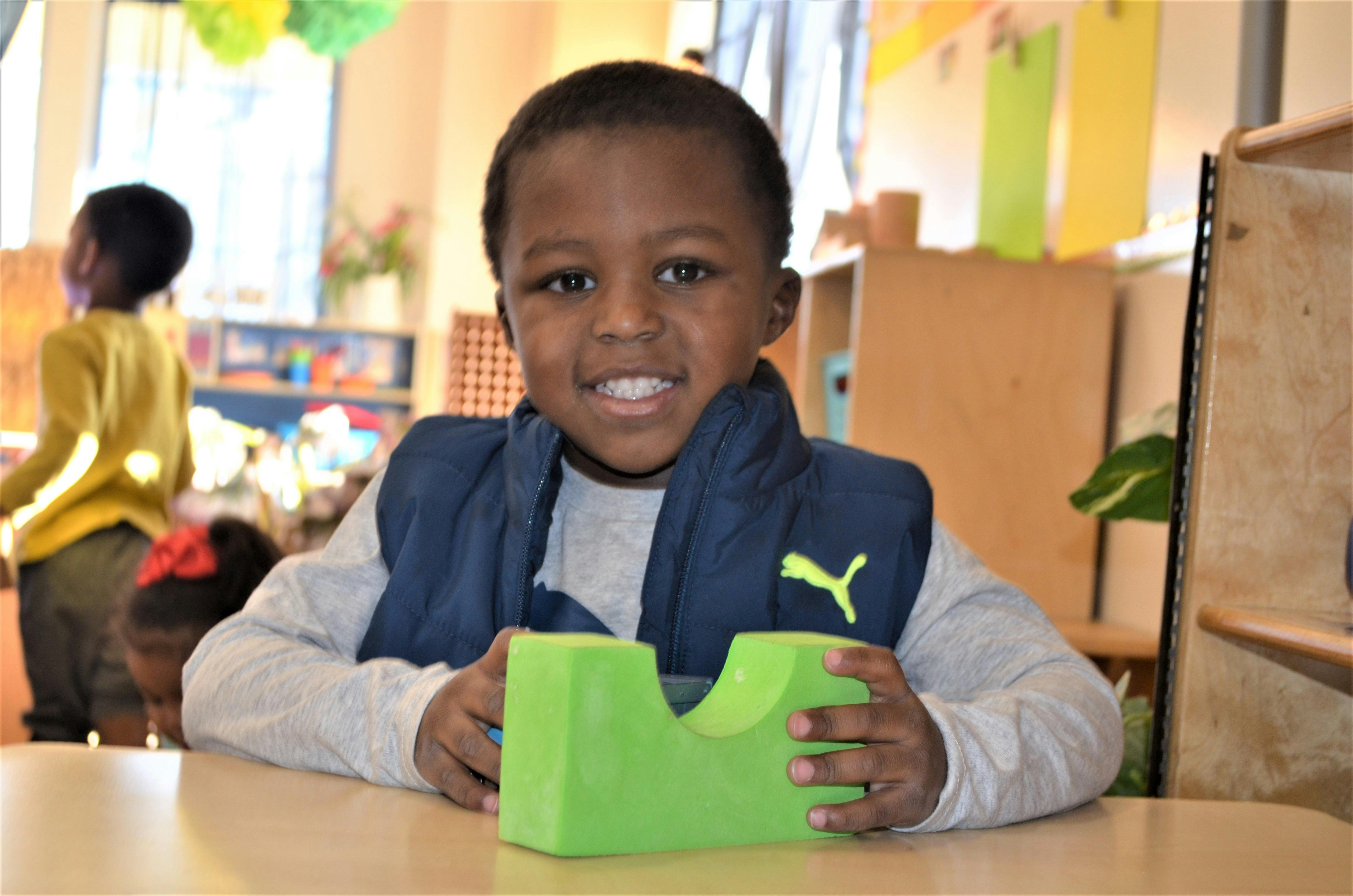 Child holding a green toy block in a classroom