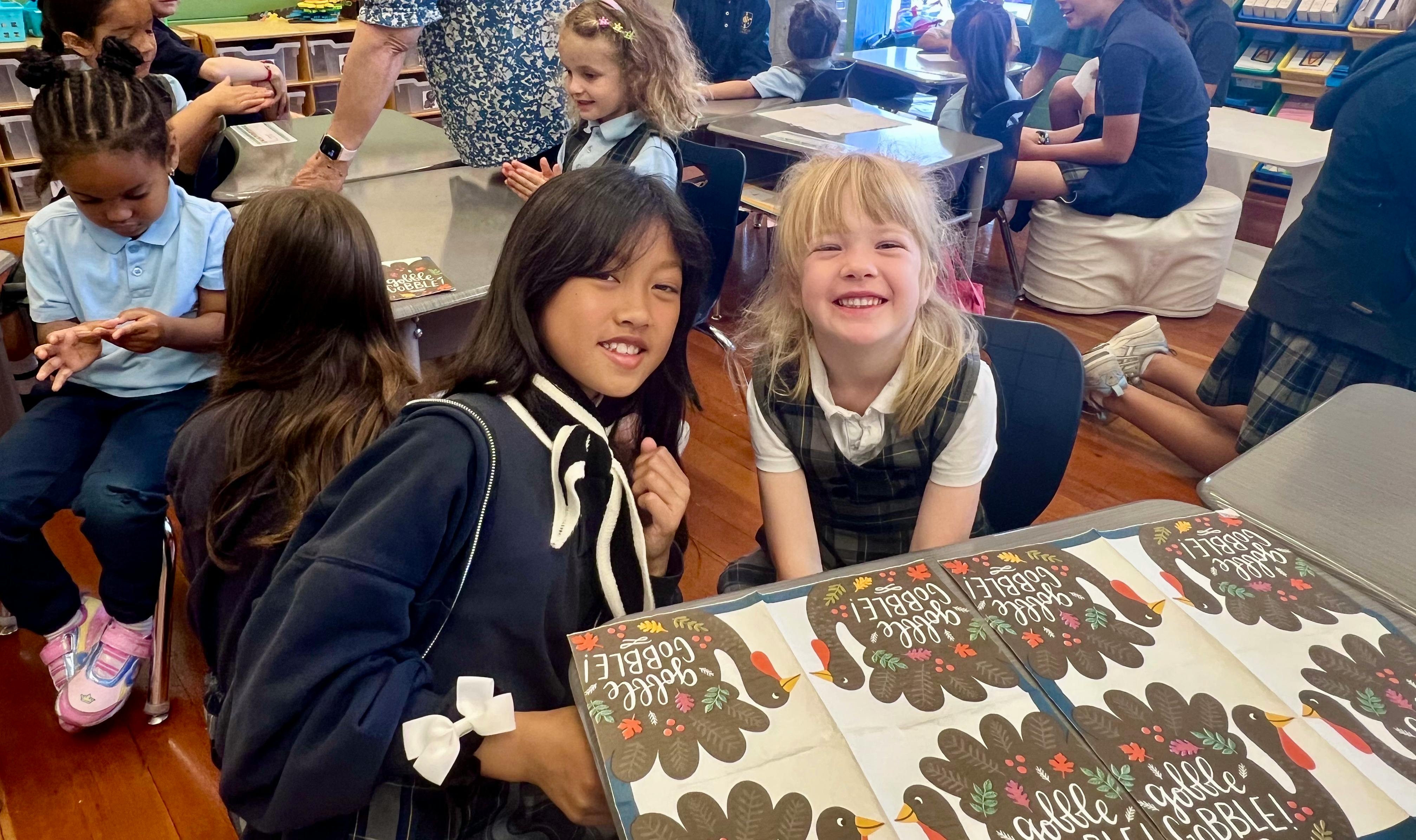 Two children smiling in a classroom with turkey crafts