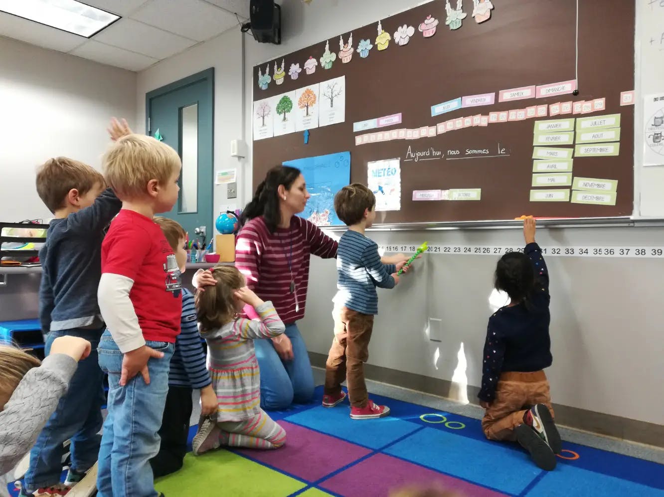 adult and children in a classroom pointing at a calendar and number line