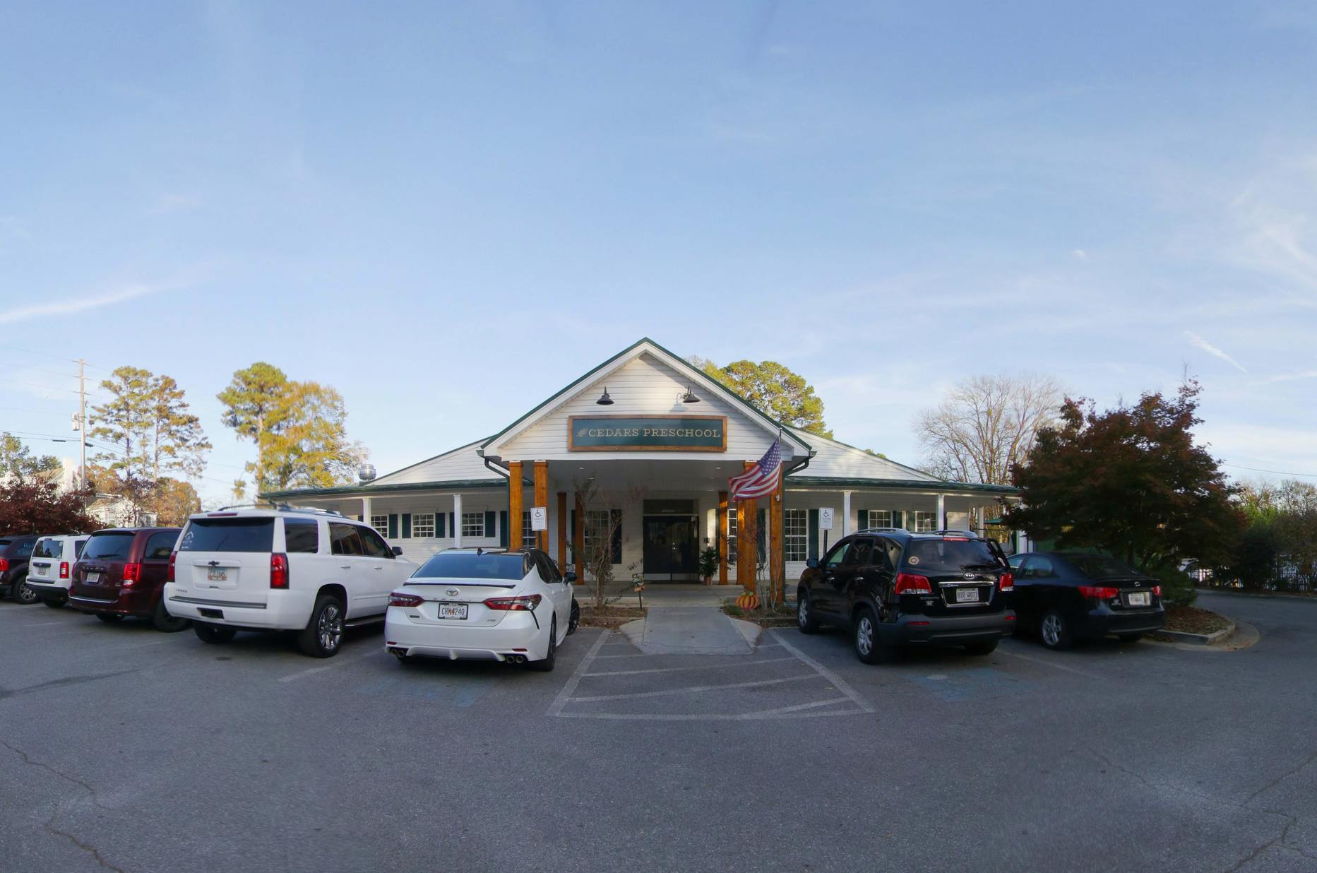 White building with sign "CEDARS PRESCHOOL" and cars parked in front