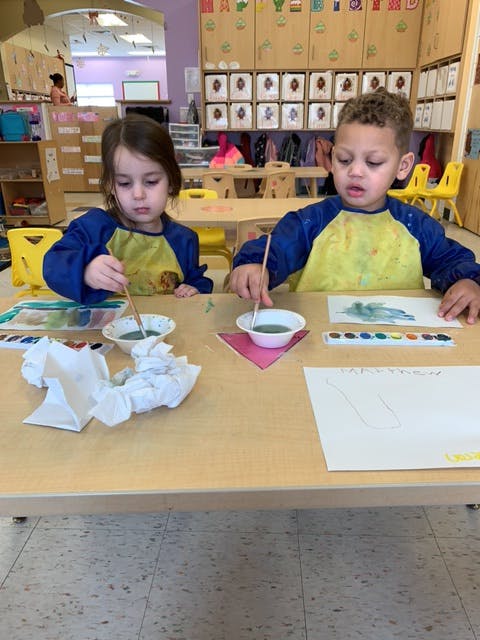 Two children painting at a table in a classroom