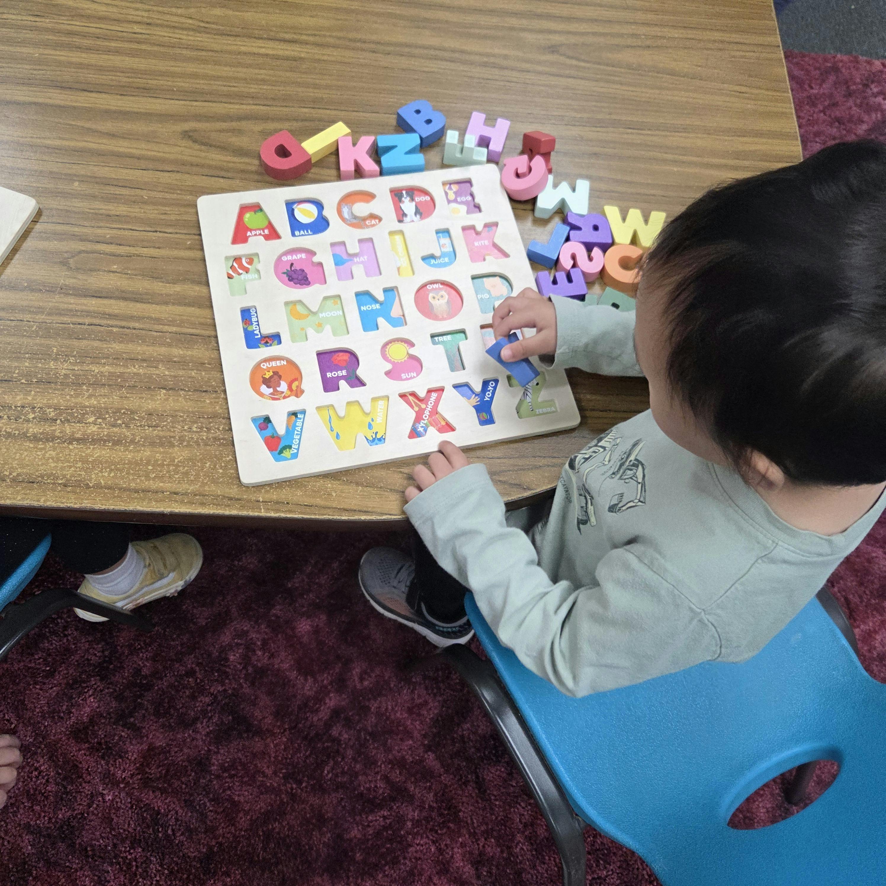 Child playing with an alphabet letter puzzle on a wooden table