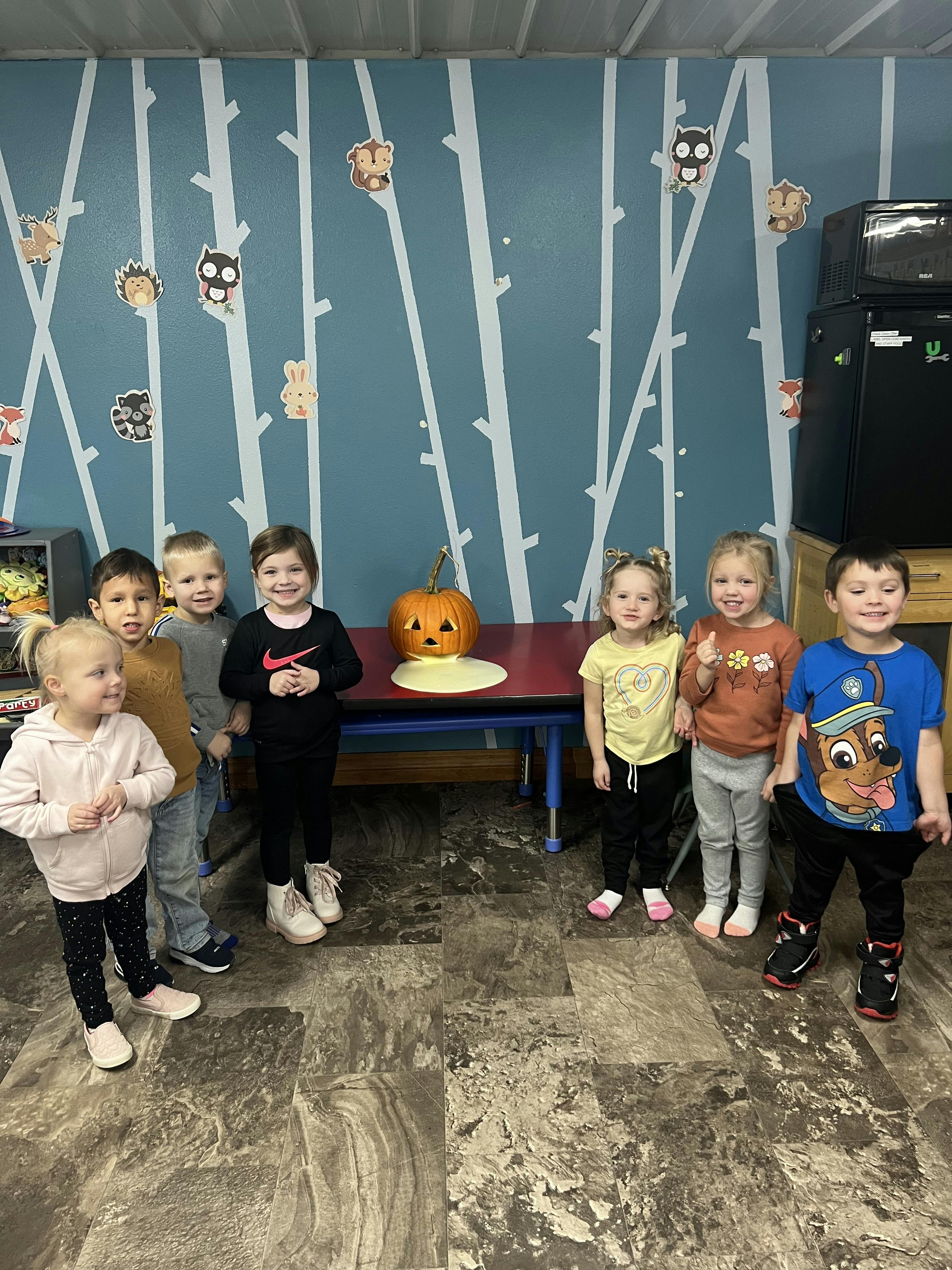 Group of children standing around a table with a carved pumpkin