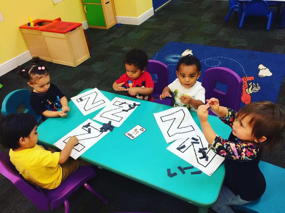 Four children sitting at a table with papers showing the letter Z