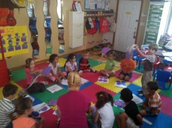 Adult and children sitting on a colorful mat in a classroom