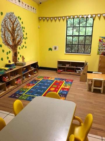 Classroom with yellow walls, tree mural, colorful rug, and small tables