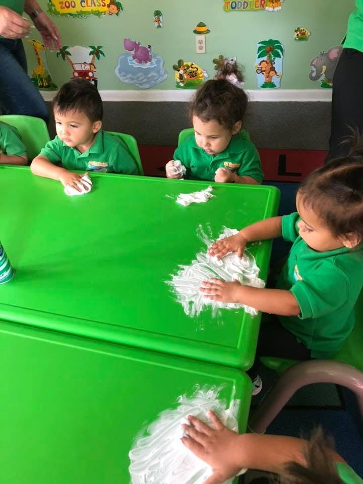 Children playing with shaving cream on green tables in a classroom