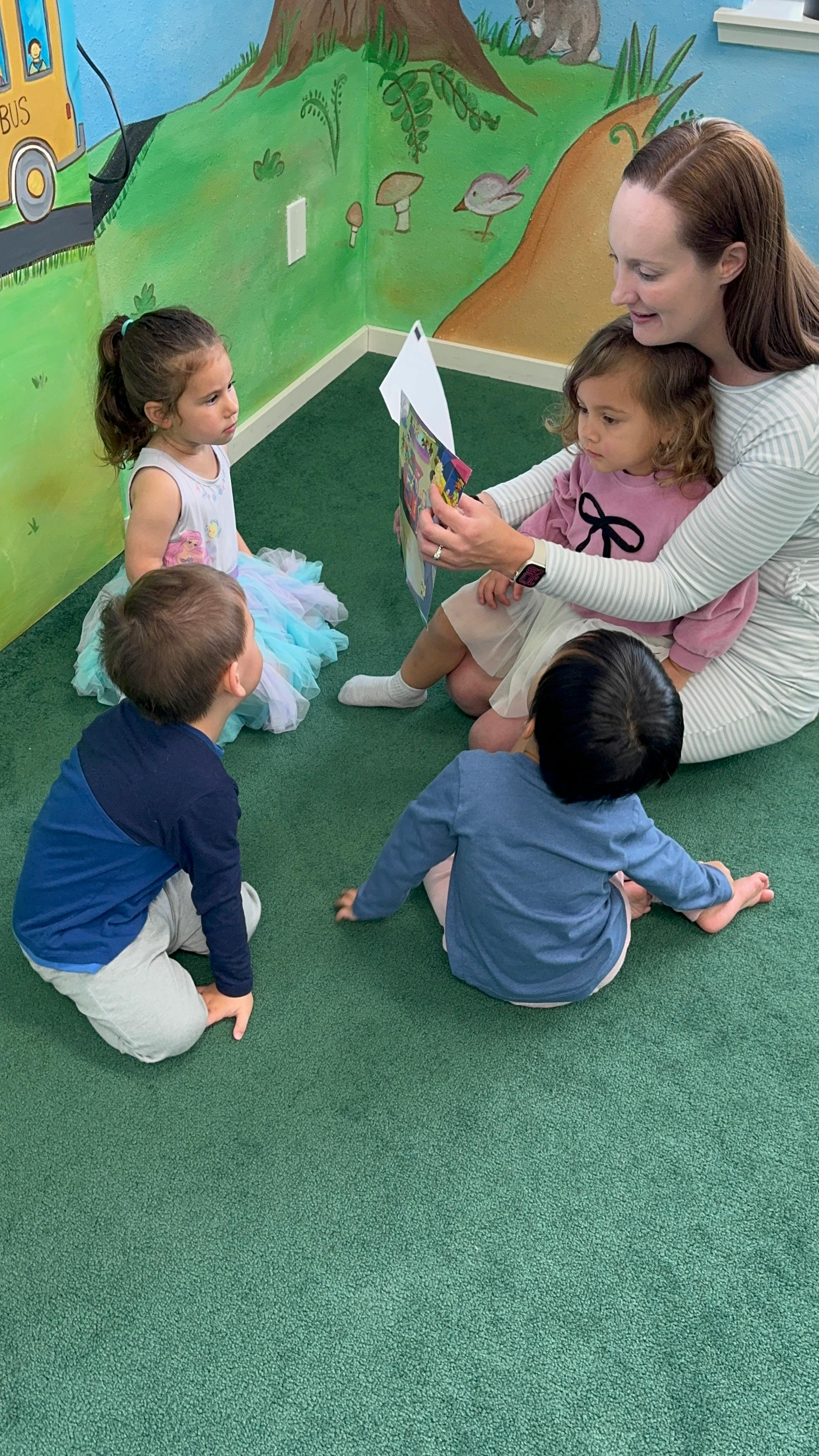 Adult reading a book to three children in a classroom