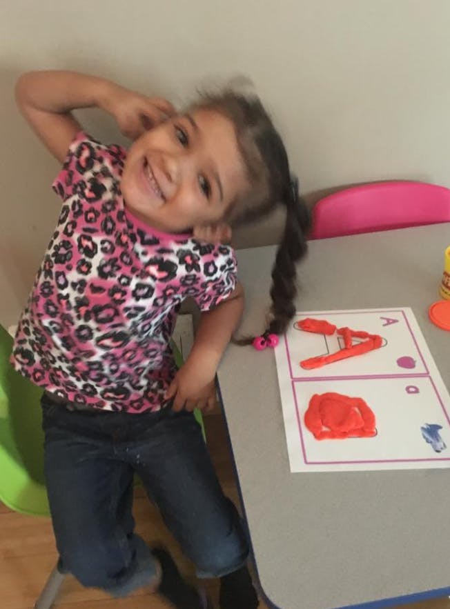 Child with braided hair sitting at a table with playdough