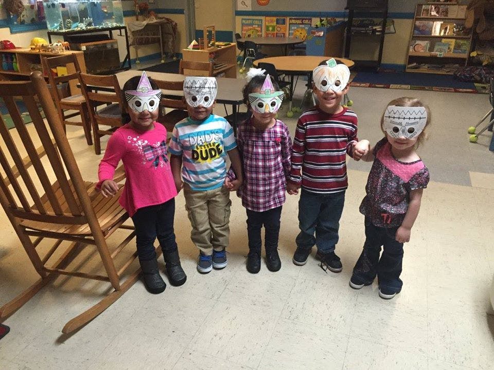 Five children wearing owl masks in a classroom