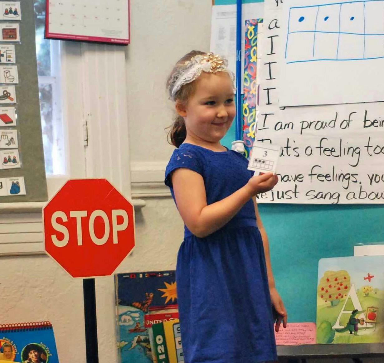 Child in a blue dress holding a card next to a STOP sign