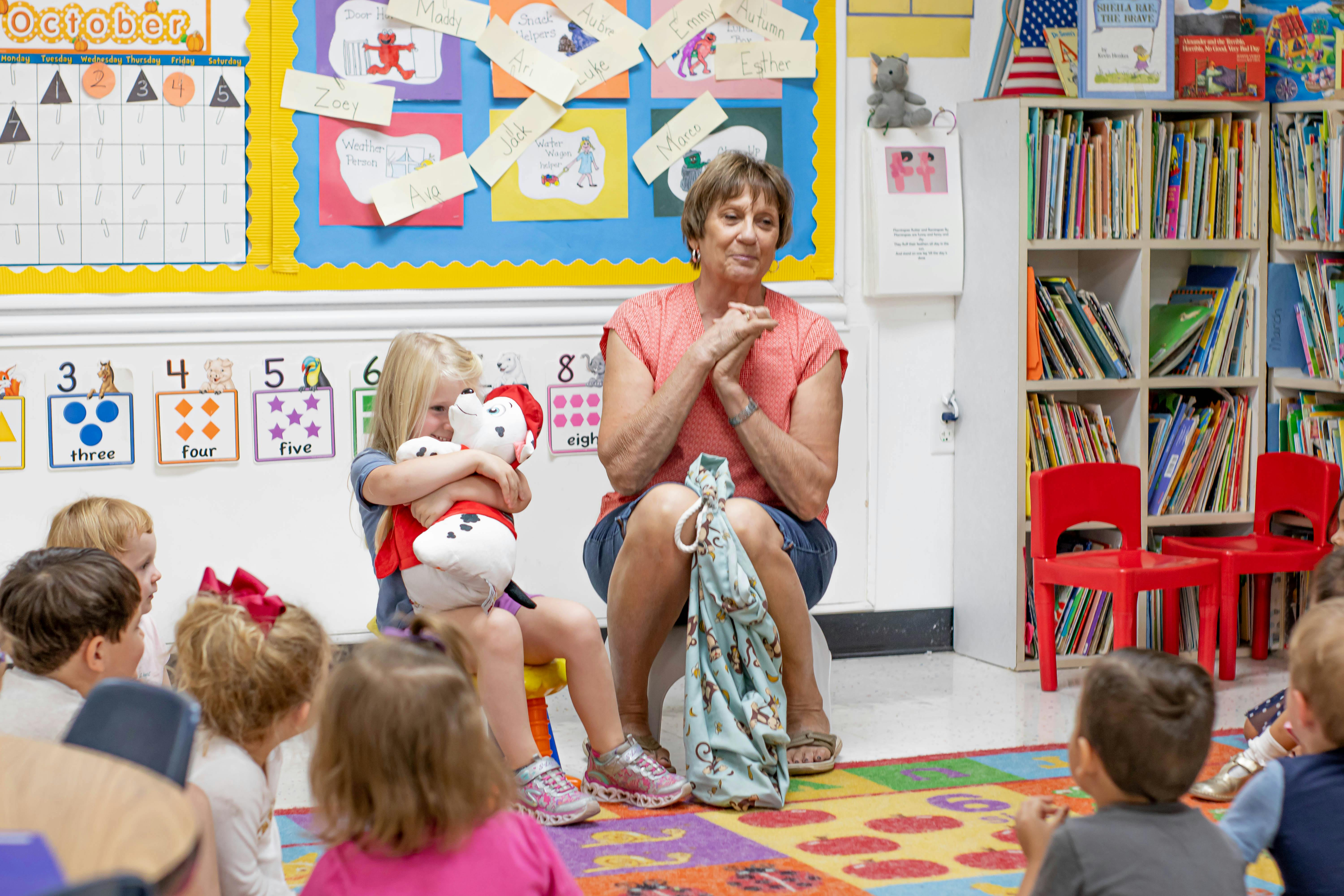 Adult and children sitting on a colorful rug in a classroom