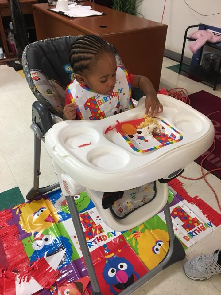 Child in a high chair with a bib, reaching for food on the tray