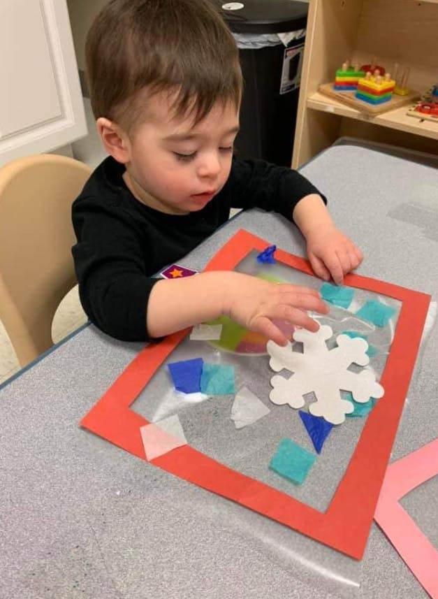 Child playing with a snowflake cutout and colorful tissue paper on a table