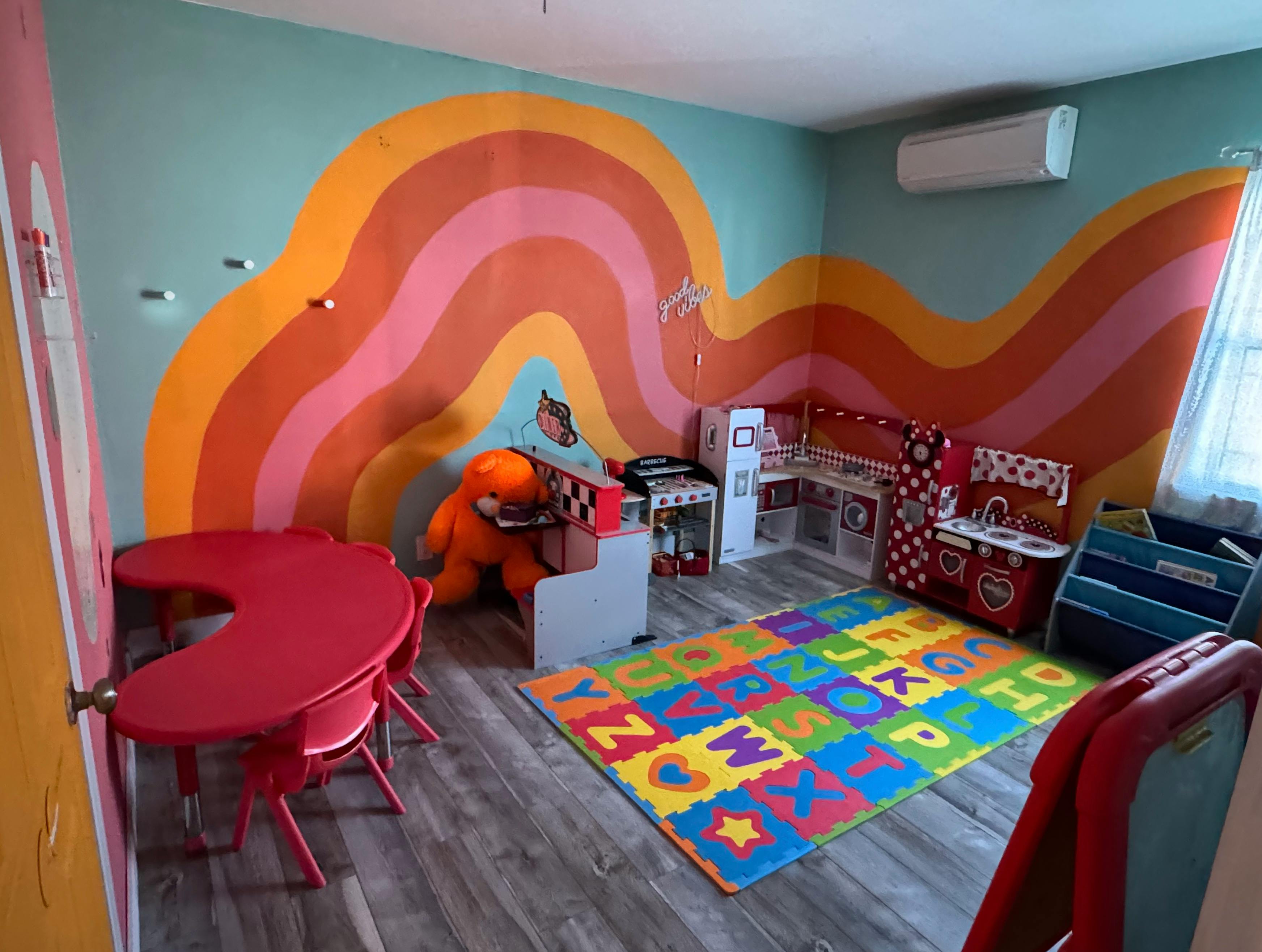 Playroom with colorful wall mural, red table, and alphabet mat