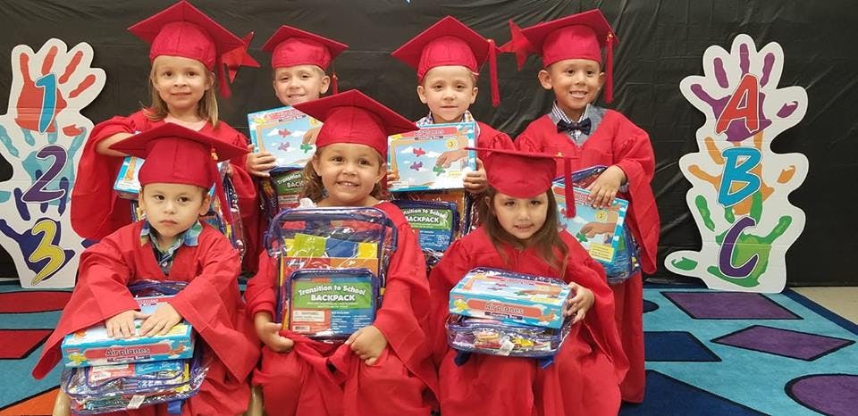 Children in red graduation caps and gowns holding books and school supplies