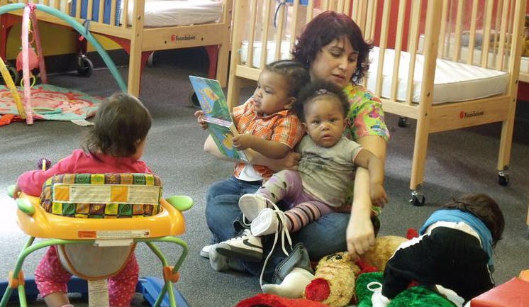 Adult and children on floor in a room with cribs