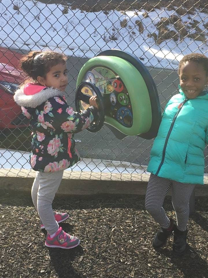 Two children playing with a toy steering wheel on a playground