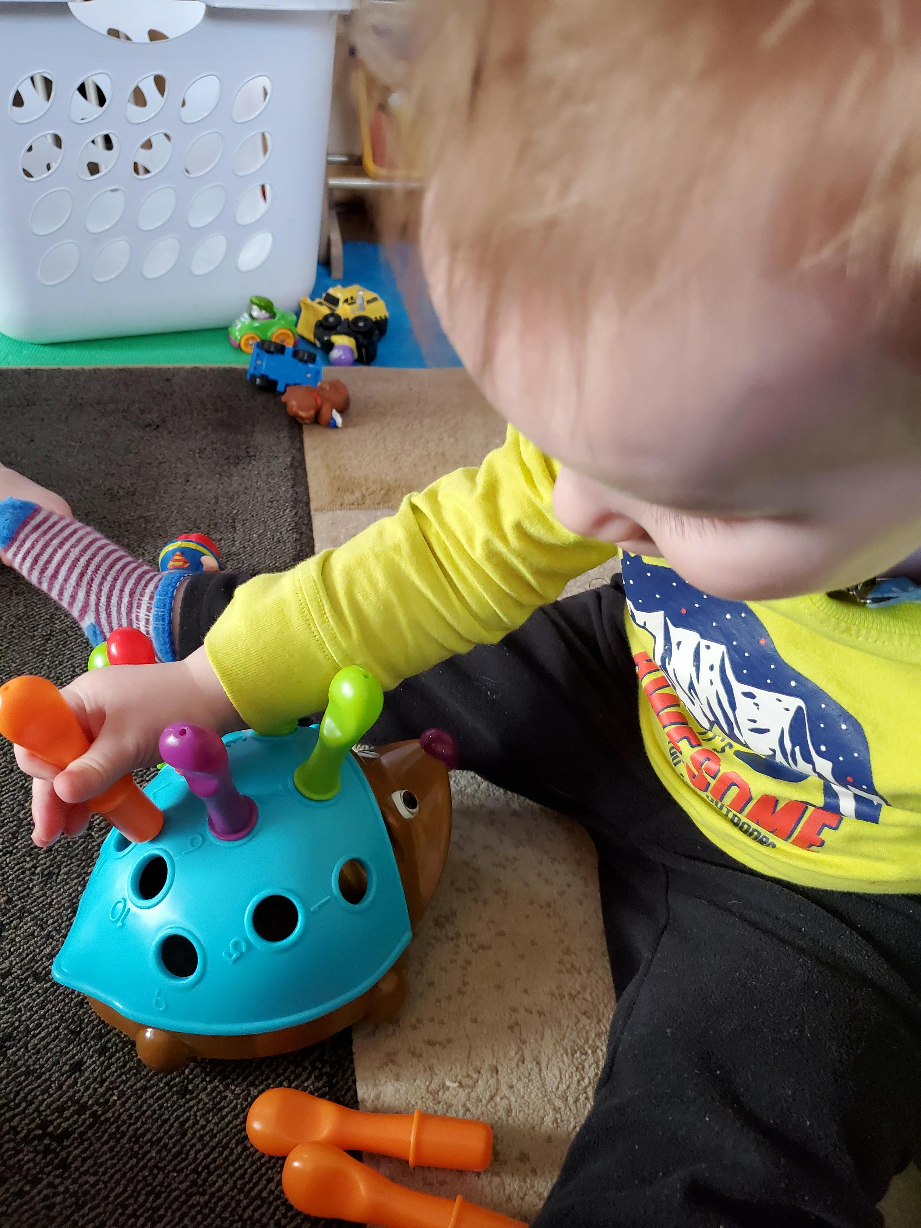 Child playing with a blue turtle-shaped toy with colorful pegs