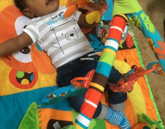 Child lying on a colorful play mat with toys