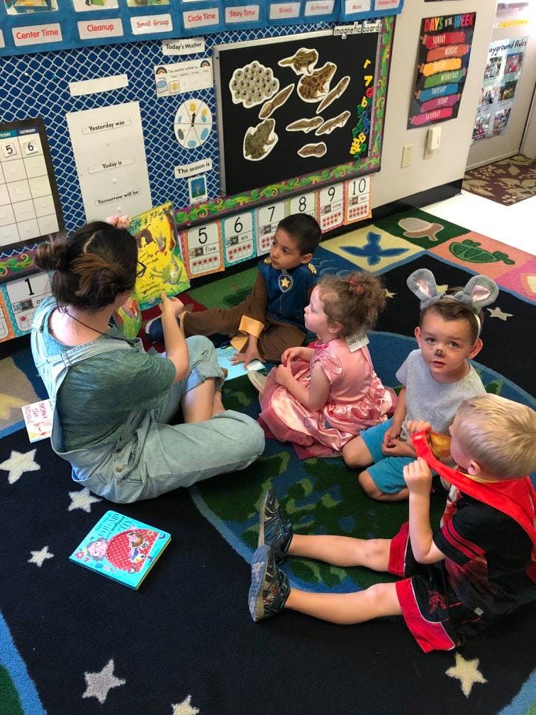 Person reading a book to four children in a classroom