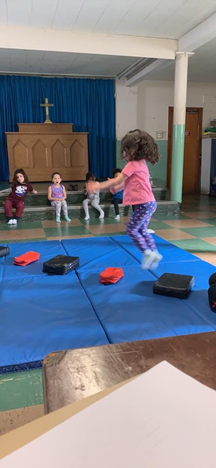 Child jumping on blue mats in a room with other children