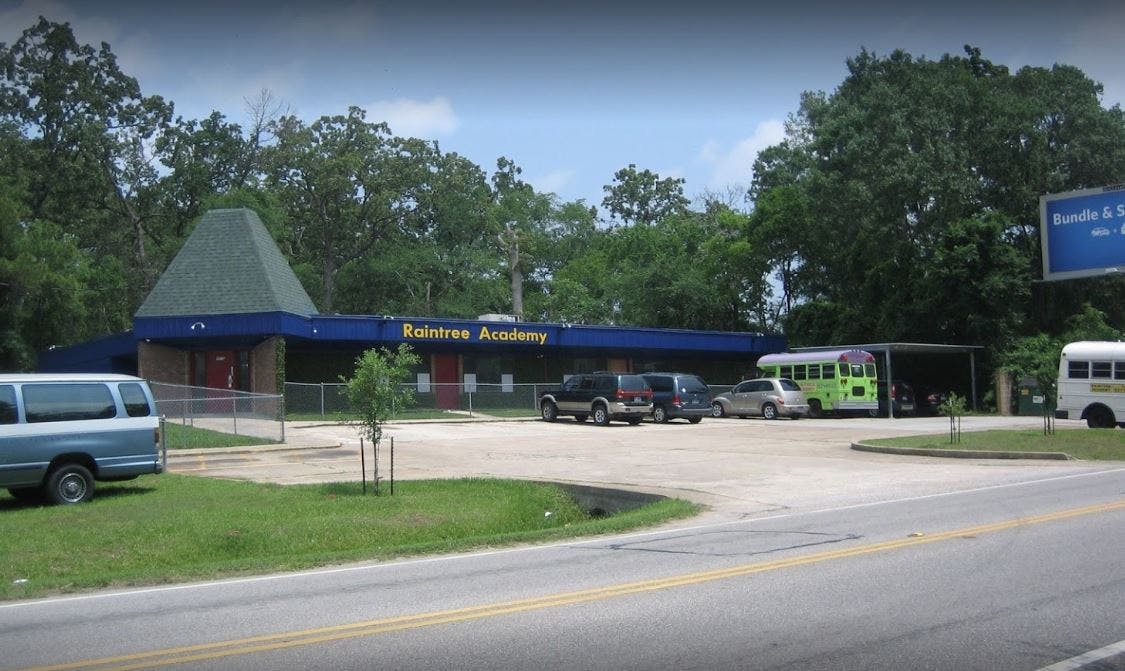 Building with a blue facade and green roof, with vehicles in a parking lot