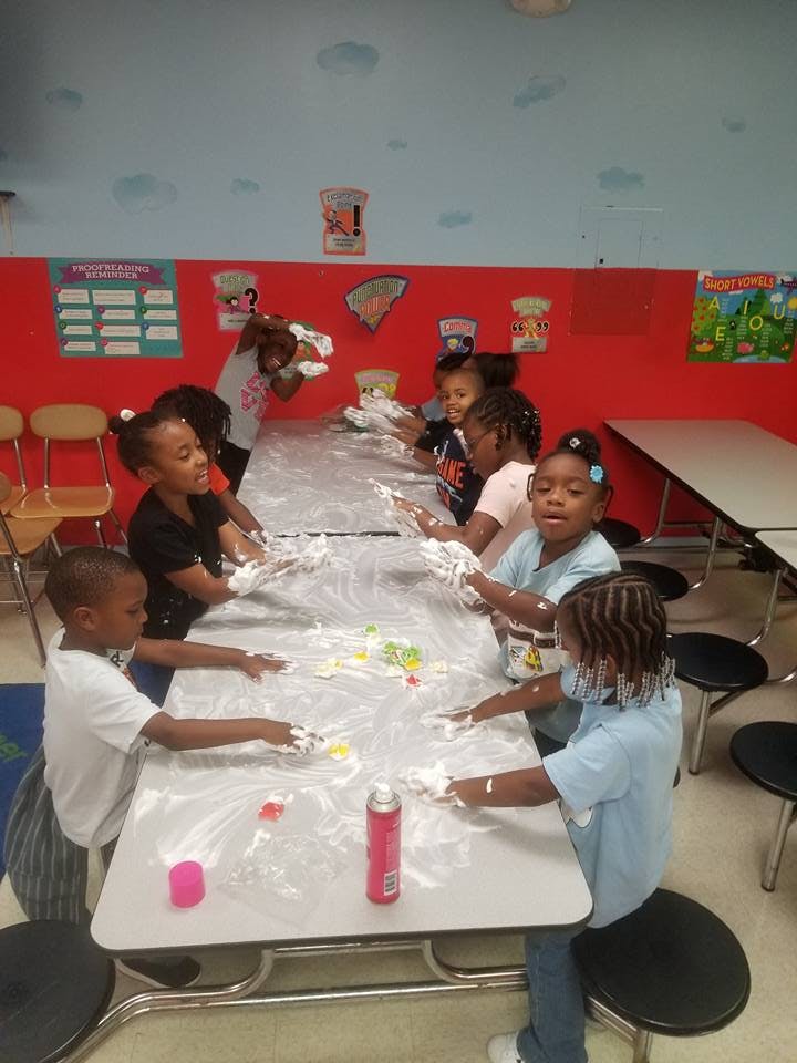 Children playing with shaving cream at a table in a classroom
