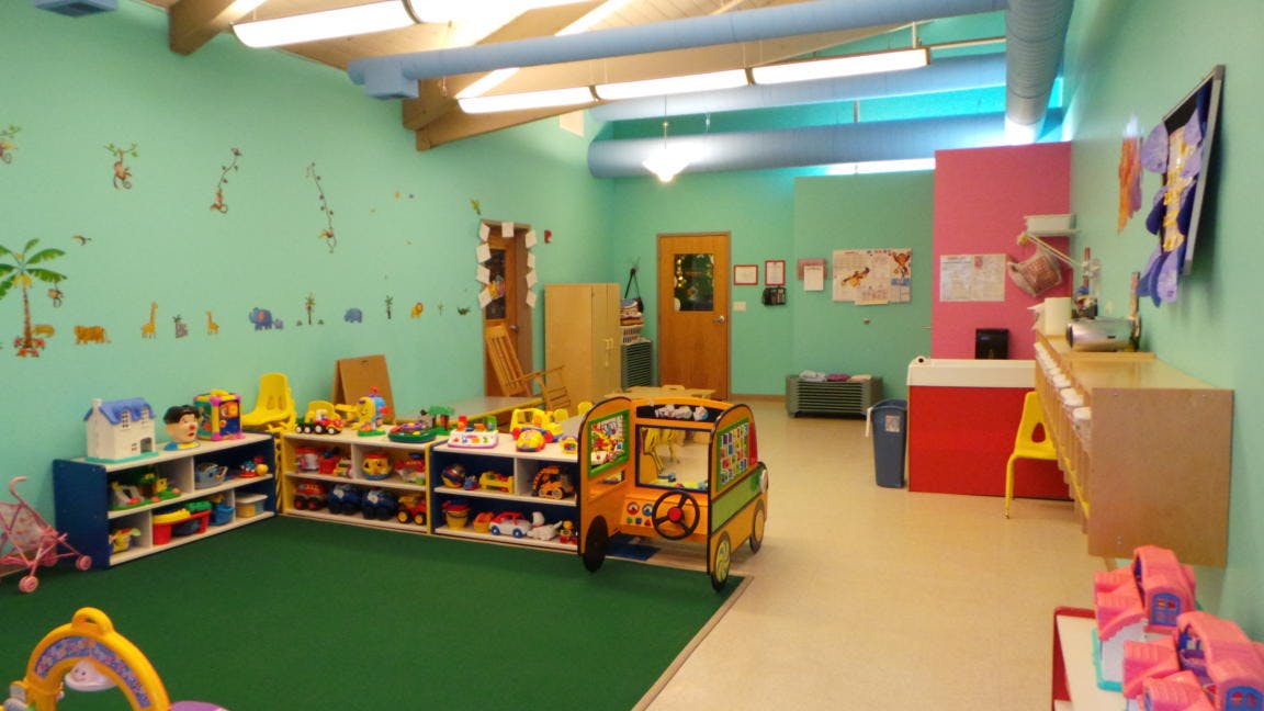 Playroom with toys on shelves and a toy bus on a green carpet