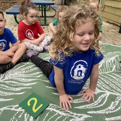 Child in blue shirt lying on a mat with other children sitting nearby
